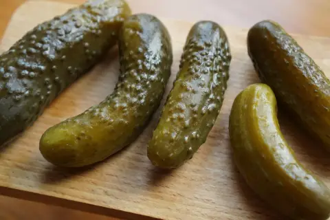 Kilka ogórków kiszonych leżących na drewnianej desce.